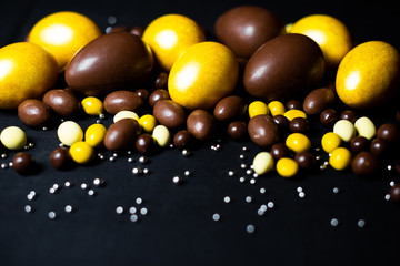 Golden eggs and delicious chocolate easter eggs and yellow sweets on black background