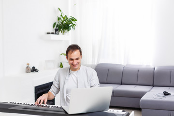 A man learning to play piano online with a computer staying at home. Concepts of self taught, staying at home and working online
