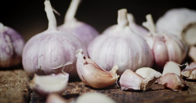 Slices of unpeeled garlic fall on the wooden table.