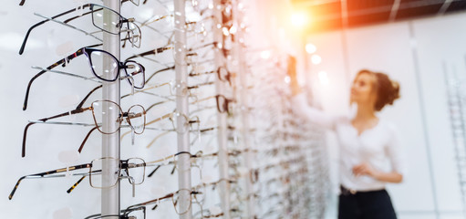 Row of glasses at an opticians. Eyeglasses shop. Stand with glasses in the store of optics. Woman chooses glasses. Presenting spectacles