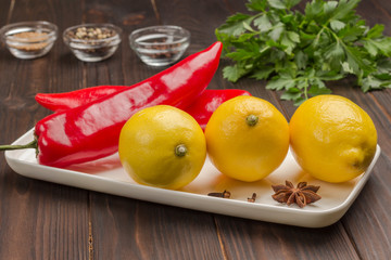 Three lemons and two chili peppers on white plate, parsley and spices.