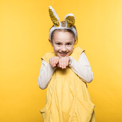 Smiling little girl with bunny ears on the yellow background
