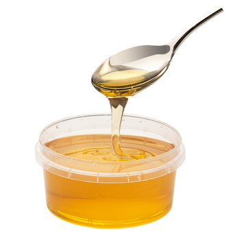honey flows from a spoon into a plastic jar