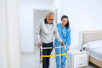 Nurse helping old man to walk with walker equipment