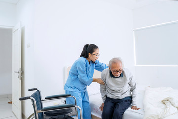 Nurse helping senior man to sit on the bed