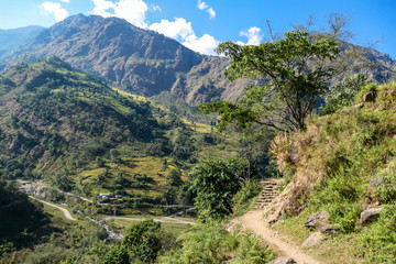 View on Himalayas along Annapurna Circuit Trek, Nepal. There is a dense forest in front. On the side there is a path way. Clouds trying to breach through the mountain range. Serenity and calmness.