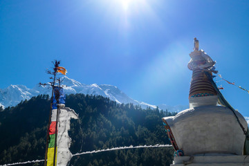A prayer flags attached to a stick waving on the wind next to a small white pagoda along Annapurna...