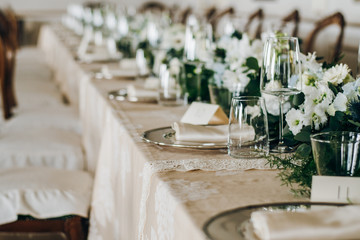 The wedding festive table is decorated with floral arrangements, glasses, plates and cutlery, the table is covered with a beautiful tablecloth