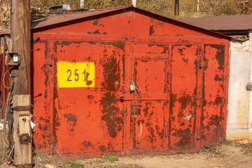 Locked with padlocks, an old metal rusty car garage with peeling red paint