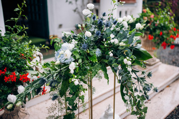 the arrangement of flowers at the wedding stands on a metal high stand, consists of many greens and white flowers