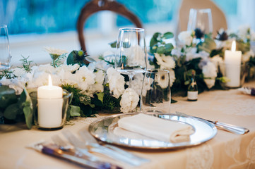 Wedding table decorated with tablecloth, fresh flowers composition, candles, plates with napkins and glasses