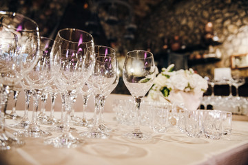 Empty wine glasses are standing on a table covere with tablecloth, there are white flowers on the background