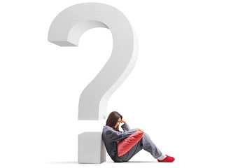 Sad young woman in pajamas sitting on the floor and leaning on a big question mark