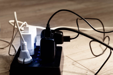 A tangle of numerous wires of electrical devices.Electrical plugs are plugged into sockets. Extension cord for power supply of devices.