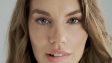 A close-up view of a seductive flirty woman is biting her lip isolated over a gray background in studio