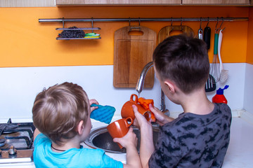 Children, two European boys washing dishes in the kitchen. Kids help mom with the housework in the kitchen.