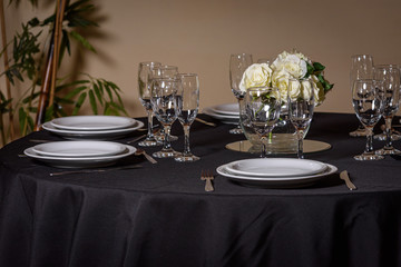 Mesa negra con platos, copas y adorno floral con rosas blancas en plano general