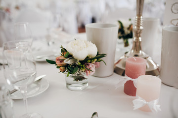 Closeup beautiful table decoration, with fresh peonies and greenery, pink candles, silver candlestick., wine glasses and plates