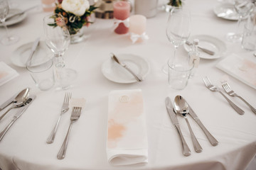 Closeup beautiful table decoration, with fresh flowers, pink candles, wine glasses and plates, menu, silverware
