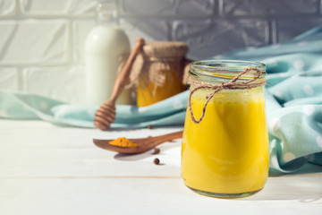 Glass jar with a healthy drink of golden milk made from turmeric, milk and pepper on a white wooden background. Prevention of diseases and viruses.