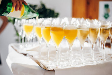Cold drink in glasses, orange juice and champagne, the waiter is pouring juice into the glass