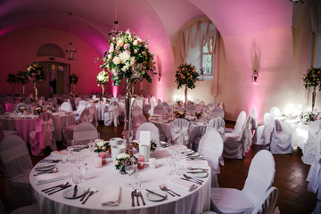 Tables for guests at the wedding, decorated with fresh flowers compositions, white tablecloth, candles, tableware