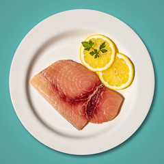Macro close-up of a plate with a slice of raw, fresh swordfish. Dish garnished with two round slices of lemon and parsley leaf. Isolated on blue background. Ready for cooking
