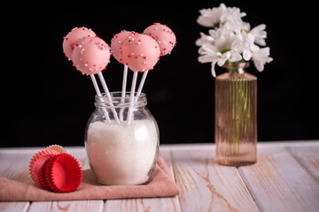 Pink cake pops in a jar of sugar in the form of a bouquet on a wooden background.