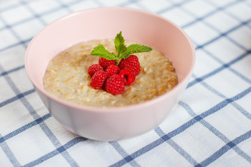 Healthy homemade oatmeal porridge with berries for breakfast in ceramic bowl on a checkered tablecloth.