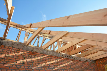 Roofing construction on the stage of roof framing, installation of wooden trusses, eaves, braces and roof beams on a brick house.