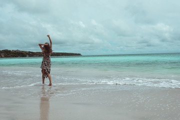 Beautiful and young girl in a dress posing on the shore of the ocean and sea with blue waves. Woman in a long dress model and fashion posing. Relax and relaxation on the island of Bali