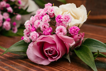 Boutonniere for the groom made of pink and cream roses, ruskus and pink gypsophila on a brown wooden table
