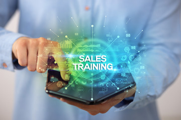 Businessman holding a foldable smartphone with SALES TRAINING inscription, new business concept