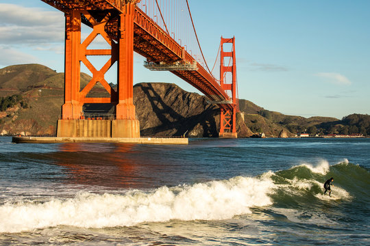 A surfer riding a wave underneath the Golden Gate Bridge during winter. 
