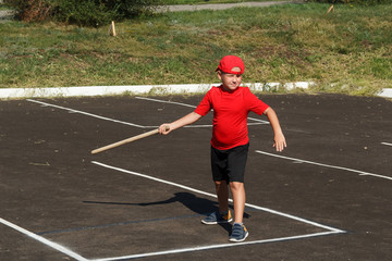 Fototapeta na wymiar an eight year old plump boy in a red t shirt and cap throws a wooden bat on the asphalt