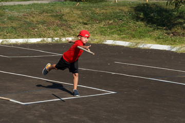 Fototapeta na wymiar a boy in a red t-shirt and cap throws a wooden bat.