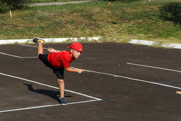Fototapeta na wymiar a boy in a red t-shirt and cap throws a wooden bat on the asphalt
