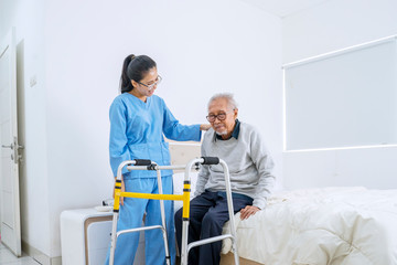 Senior man sitting on bed and nurse helping him