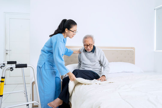 Senior man sitting on the bed helped by nurse