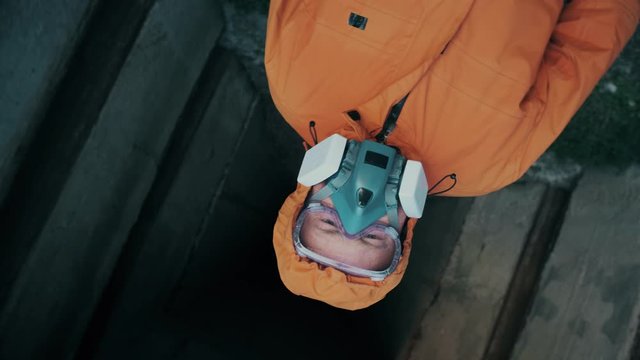 A man in a respirator with goggles and in a special overalls of bright red color comes out of the concrete shelter, meanwhile the camera on the stabilizer rotates around its axis.