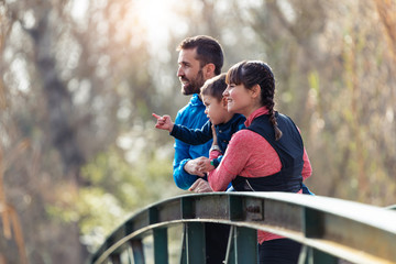 Happy young family looking at the pond from the bridge while enjoying the time together.