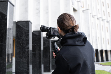 Young Professional videographer holding professional camera on 3-axis gimbal stabilizer. Pro equipment helps to make high quality video without shaking. Cameraman wearing black hoodie making a videos. © Volodymyr_sh