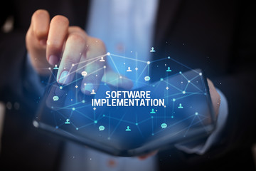 Businessman holding a foldable smartphone with SOFTWARE IMPLEMENTATION inscription, new technology concept