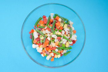 Shredded frozen vegetables in a glass bowl on a blue background. Horizontal orientation. View from above.