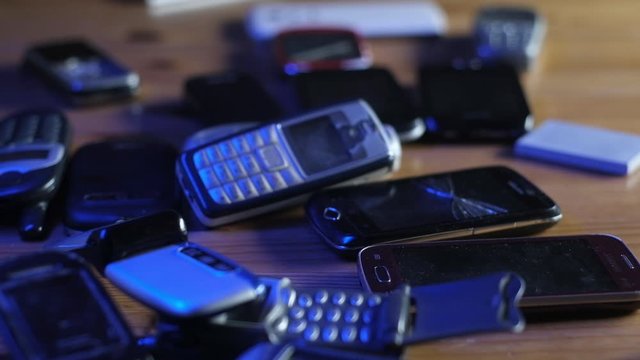 Analog communication. Old broken dusty cell phones lie on table in neon light.
