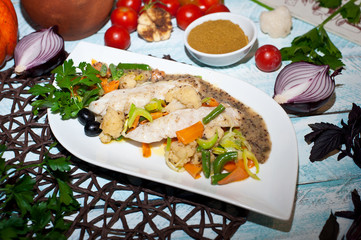 food photo steamed fish with vegetables on a white plate with onion halves tomatoes green branches on a blue wooden background