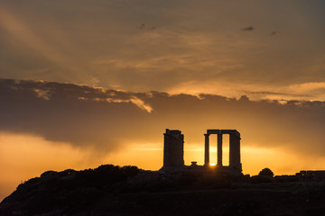 Obraz premium The silhouette of the famous ancient temple of Poseidon in Cape Sounio near Athens Greece during sunset with beautiful sun rays and warm orange light