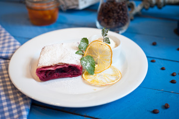 cherry strudel on a white plate with lemon on a blue wooden background raspberry sauce on a white plate