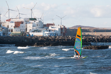 A windsurfer is racing with a little town with windmills in background