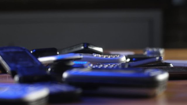 Analog communication in office. Old broken scratched and dusty cell phones lie in  pile on table in neon light.  Modern wireless technology. Recycling of retro electronics. Close-up of old and phone.